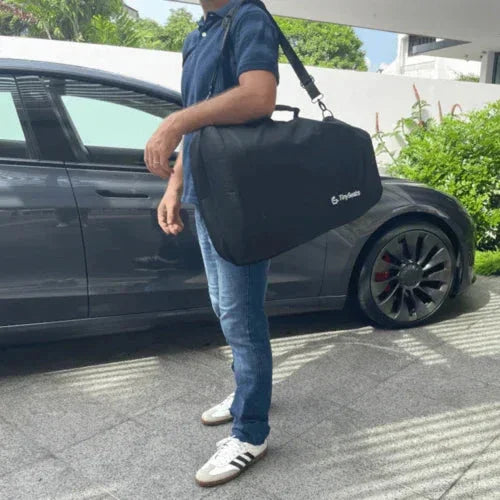 Man is carrying a TinySeats Shoulder Bag with a TinySeats inside. He is walking next to a Tesla on a driveway in Singapore