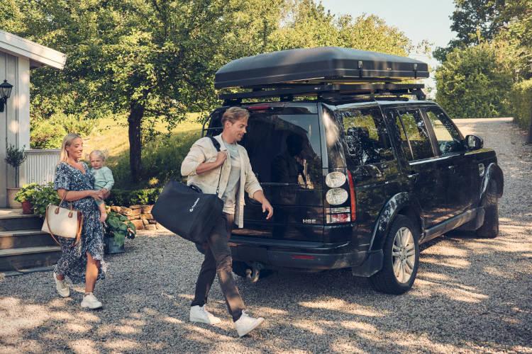 Man walking with a compact carseat hanging over his shoulder with wife and baby following behind