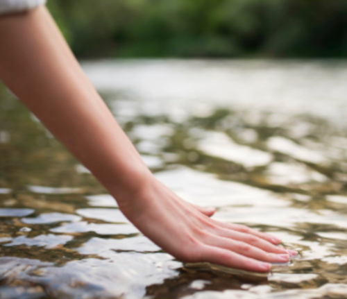 Hand touching water with a blurred natural background